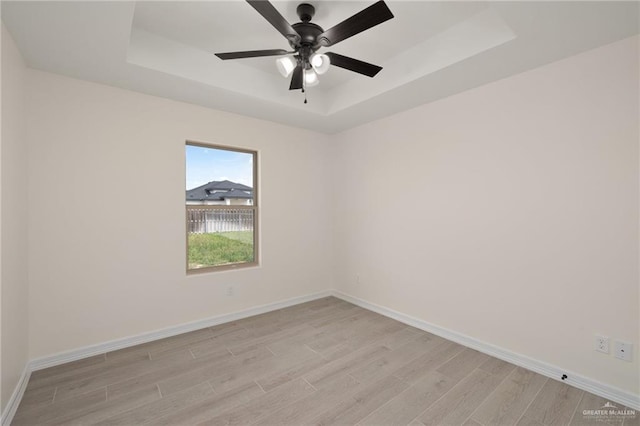 empty room featuring a tray ceiling, ceiling fan, and light hardwood / wood-style floors