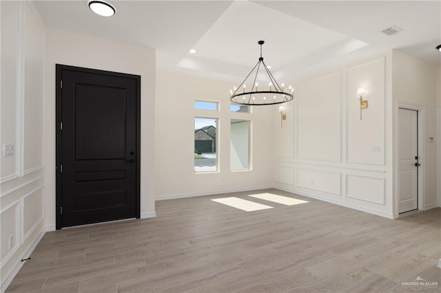 unfurnished dining area featuring light hardwood / wood-style floors, a raised ceiling, and a notable chandelier