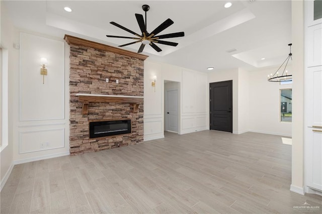 unfurnished living room featuring a fireplace, a raised ceiling, ceiling fan with notable chandelier, and light hardwood / wood-style flooring