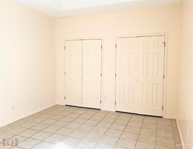 unfurnished bedroom featuring light tile patterned floors and two closets