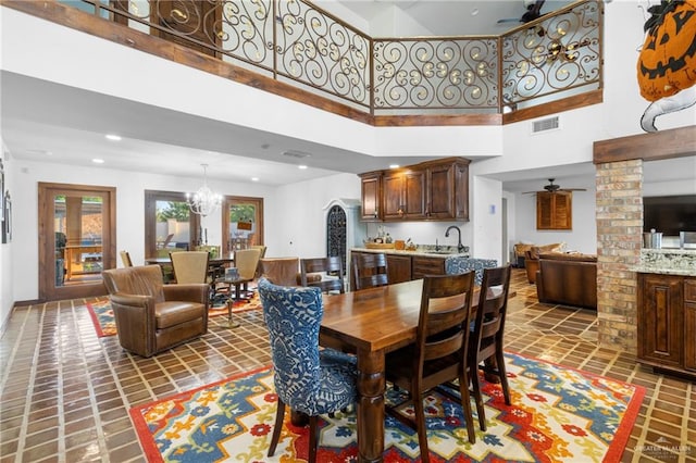 dining space with ceiling fan with notable chandelier, a towering ceiling, and sink