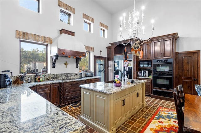 kitchen with a kitchen island with sink, a chandelier, black appliances, and light stone counters