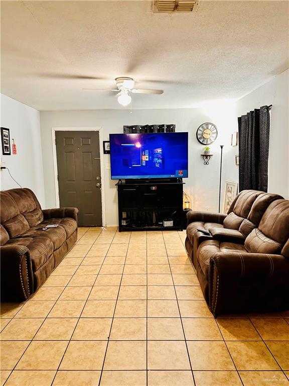 living room with ceiling fan, light tile patterned floors, and a textured ceiling