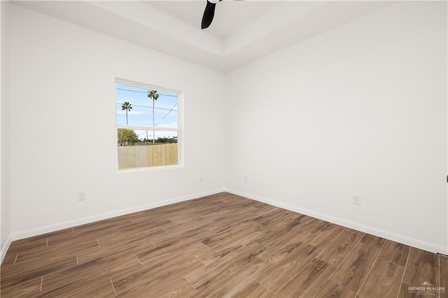 empty room featuring a raised ceiling, wood finished floors, baseboards, and ceiling fan