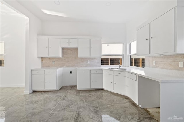 kitchen featuring light countertops, tasteful backsplash, a sink, and white cabinets