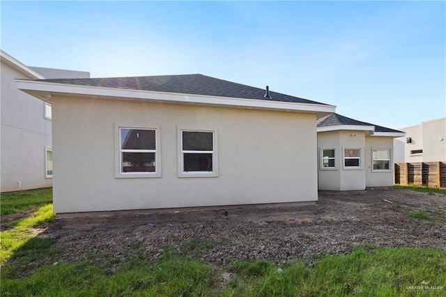 rear view of house with roof with shingles and stucco siding