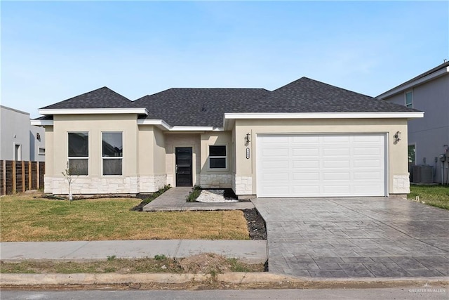 view of front of house featuring decorative driveway, roof with shingles, central air condition unit, a garage, and stone siding