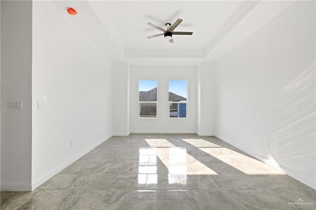 unfurnished room with a ceiling fan, a tray ceiling, marble finish floor, and baseboards