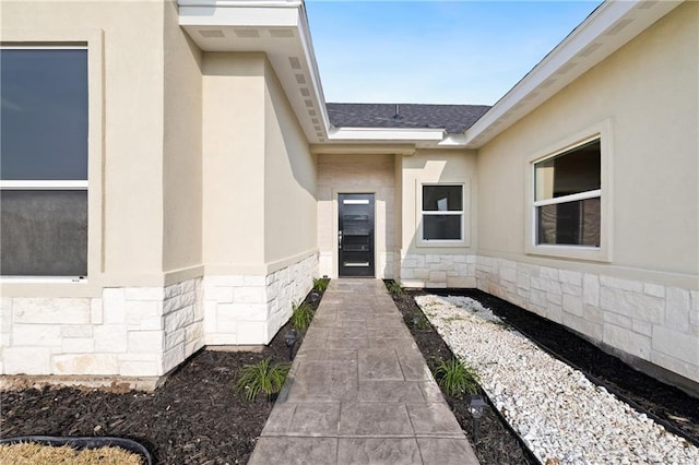 entrance to property with stone siding, a shingled roof, and stucco siding