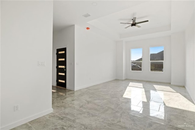 spare room with a ceiling fan, a raised ceiling, visible vents, and baseboards