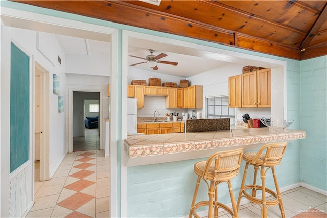 kitchen with kitchen peninsula, vaulted ceiling, sink, white refrigerator, and a breakfast bar area