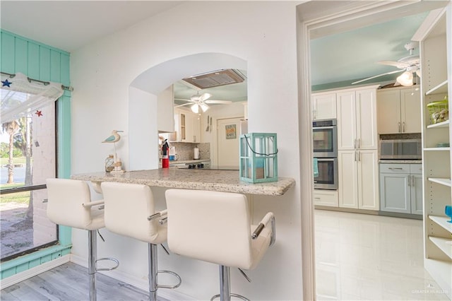 kitchen featuring light stone countertops, decorative backsplash, a breakfast bar, and stainless steel double oven