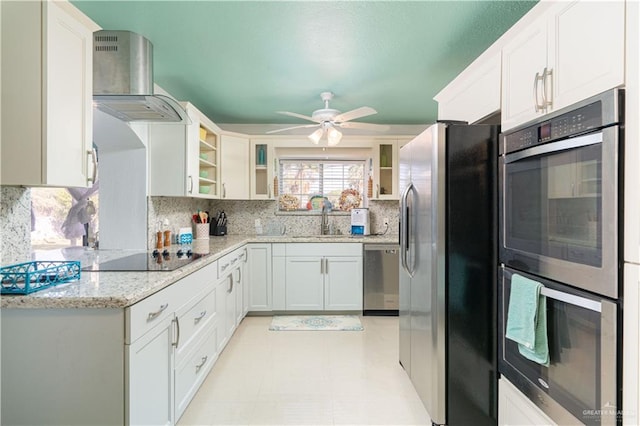 kitchen featuring appliances with stainless steel finishes, light stone counters, wall chimney exhaust hood, sink, and white cabinets