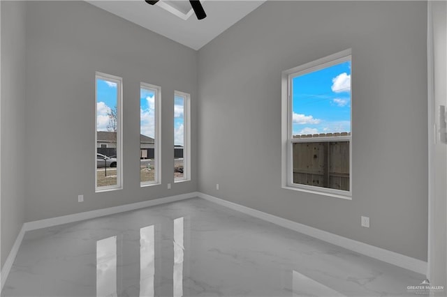 spare room with baseboards, marble finish floor, ceiling fan, and a healthy amount of sunlight