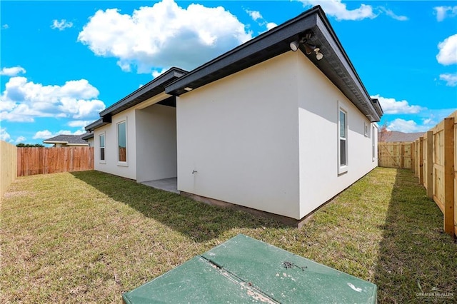 view of side of home featuring a fenced backyard, a lawn, and stucco siding