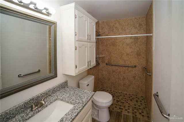 bathroom with a tile shower, vanity, wood-type flooring, and toilet