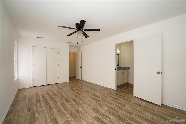 unfurnished bedroom with ceiling fan, light wood-type flooring, ensuite bathroom, and a closet