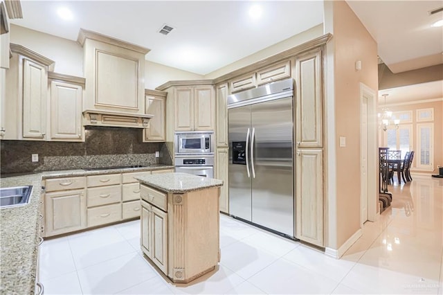 kitchen with a center island, tasteful backsplash, light stone counters, built in appliances, and a chandelier