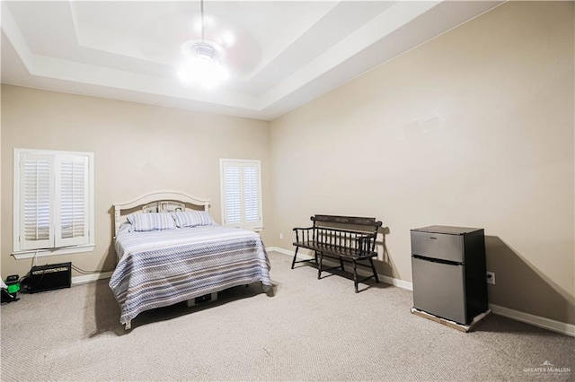 carpeted bedroom with ceiling fan, a raised ceiling, and stainless steel refrigerator