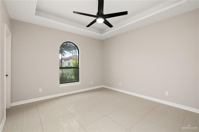 tiled empty room with a raised ceiling and ceiling fan