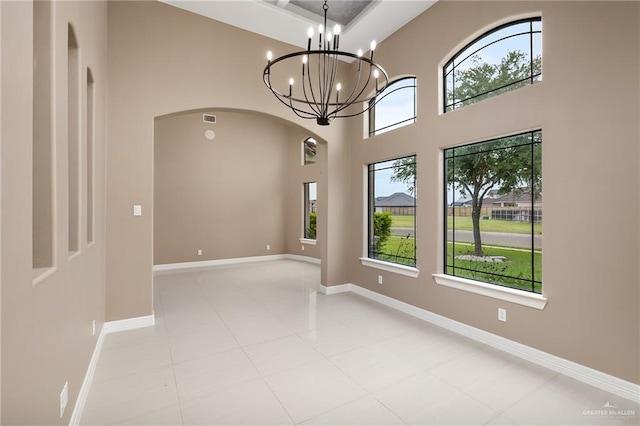 empty room featuring a chandelier, a high ceiling, light tile patterned floors, and a wealth of natural light