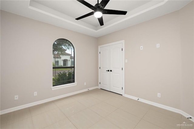 empty room with a tray ceiling, ceiling fan, and light tile patterned flooring