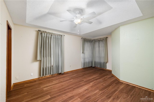 empty room featuring a raised ceiling, ceiling fan, and dark hardwood / wood-style flooring