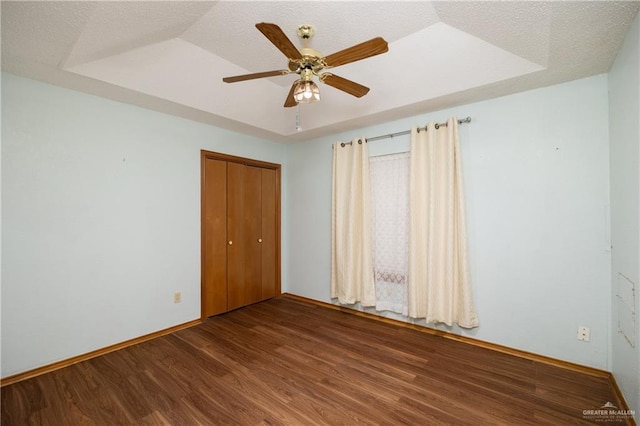 unfurnished bedroom with hardwood / wood-style floors, a tray ceiling, a closet, and ceiling fan