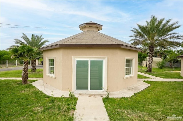 rear view of house featuring a lawn and stucco siding
