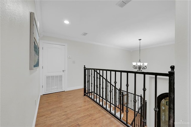 corridor featuring wood finished floors, an upstairs landing, visible vents, ornamental molding, and an inviting chandelier