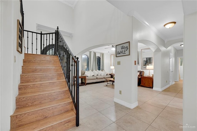 stairs with ornamental molding, arched walkways, ceiling fan, and tile patterned floors