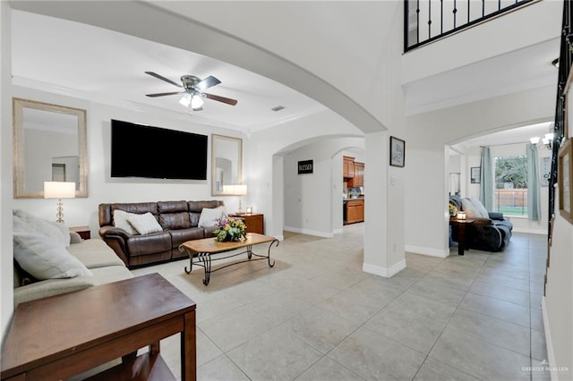 living area featuring arched walkways, light tile patterned flooring, a ceiling fan, baseboards, and crown molding