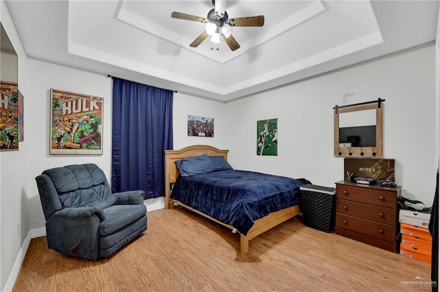 bedroom featuring wood finished floors, a raised ceiling, a ceiling fan, and baseboards