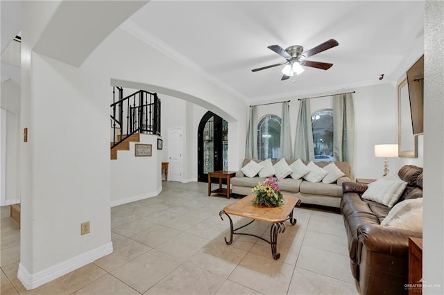 living room featuring arched walkways, ceiling fan, stairway, ornamental molding, and light tile patterned flooring