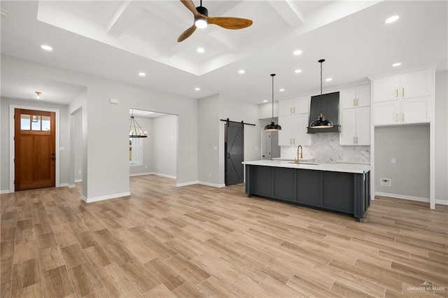 kitchen featuring sink, white cabinetry, decorative light fixtures, an island with sink, and a barn door