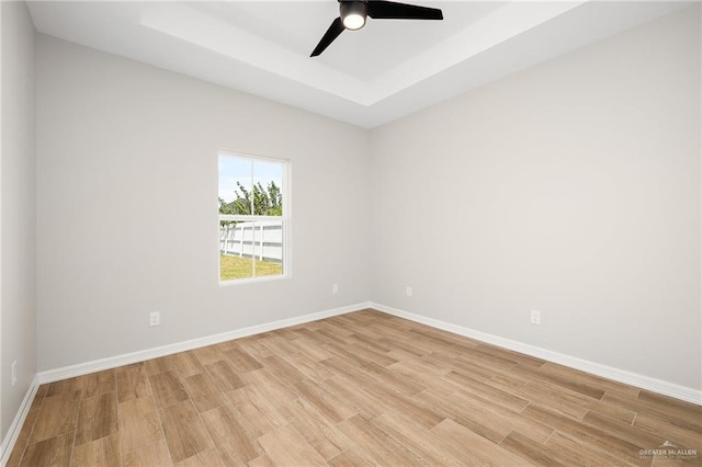 empty room featuring a tray ceiling, light hardwood / wood-style floors, and ceiling fan