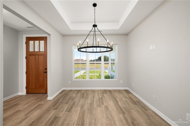 unfurnished dining area with wood-type flooring, a notable chandelier, and a tray ceiling