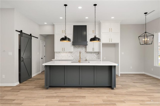 kitchen with white cabinets, an island with sink, a barn door, and wall chimney exhaust hood