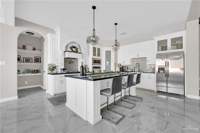 kitchen with pendant lighting, appliances with stainless steel finishes, white cabinetry, tasteful backsplash, and a center island with sink