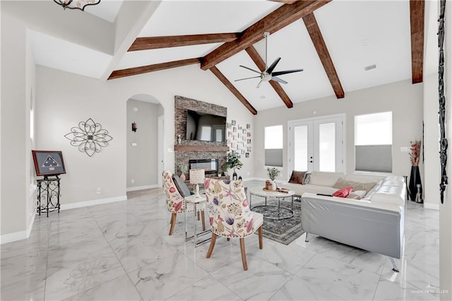 living room with ceiling fan, beam ceiling, high vaulted ceiling, a stone fireplace, and french doors