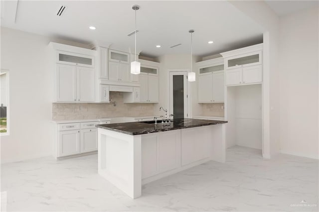 kitchen with backsplash, white cabinets, and an island with sink