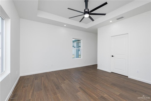 empty room with dark hardwood / wood-style flooring, a tray ceiling, and ceiling fan