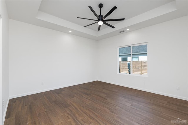 spare room featuring a raised ceiling, ceiling fan, and dark wood-type flooring