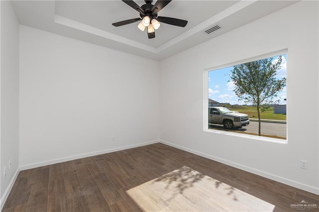 spare room with dark hardwood / wood-style flooring, a tray ceiling, and ceiling fan