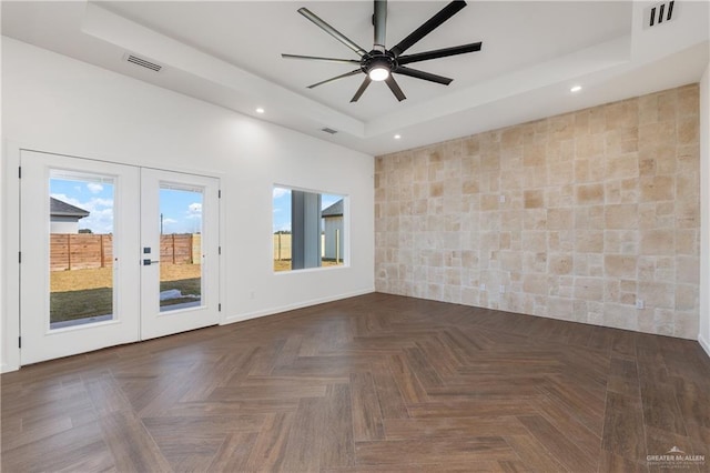 spare room with ceiling fan, dark parquet flooring, a tray ceiling, and french doors