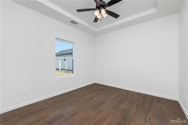 empty room with dark hardwood / wood-style flooring, a raised ceiling, and ceiling fan