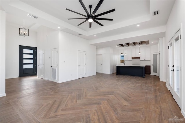 unfurnished living room featuring a tray ceiling, sink, parquet floors, and ceiling fan with notable chandelier