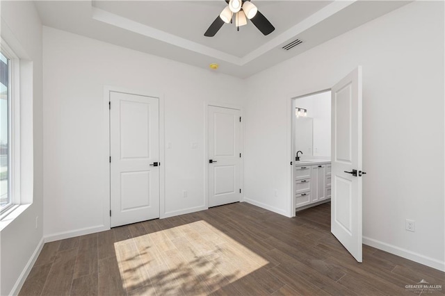 unfurnished bedroom featuring ensuite bathroom, a raised ceiling, ceiling fan, and dark hardwood / wood-style floors