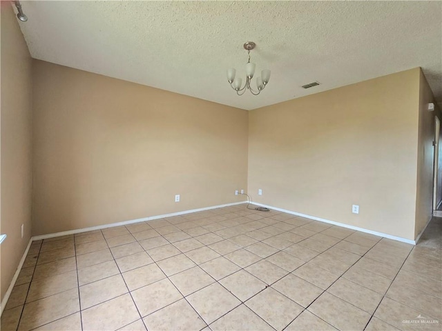 tiled empty room with a textured ceiling and a notable chandelier