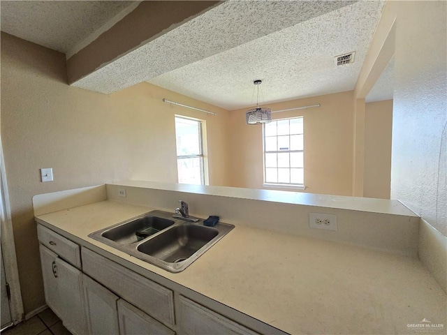 kitchen featuring sink, tile patterned flooring, kitchen peninsula, a textured ceiling, and decorative light fixtures